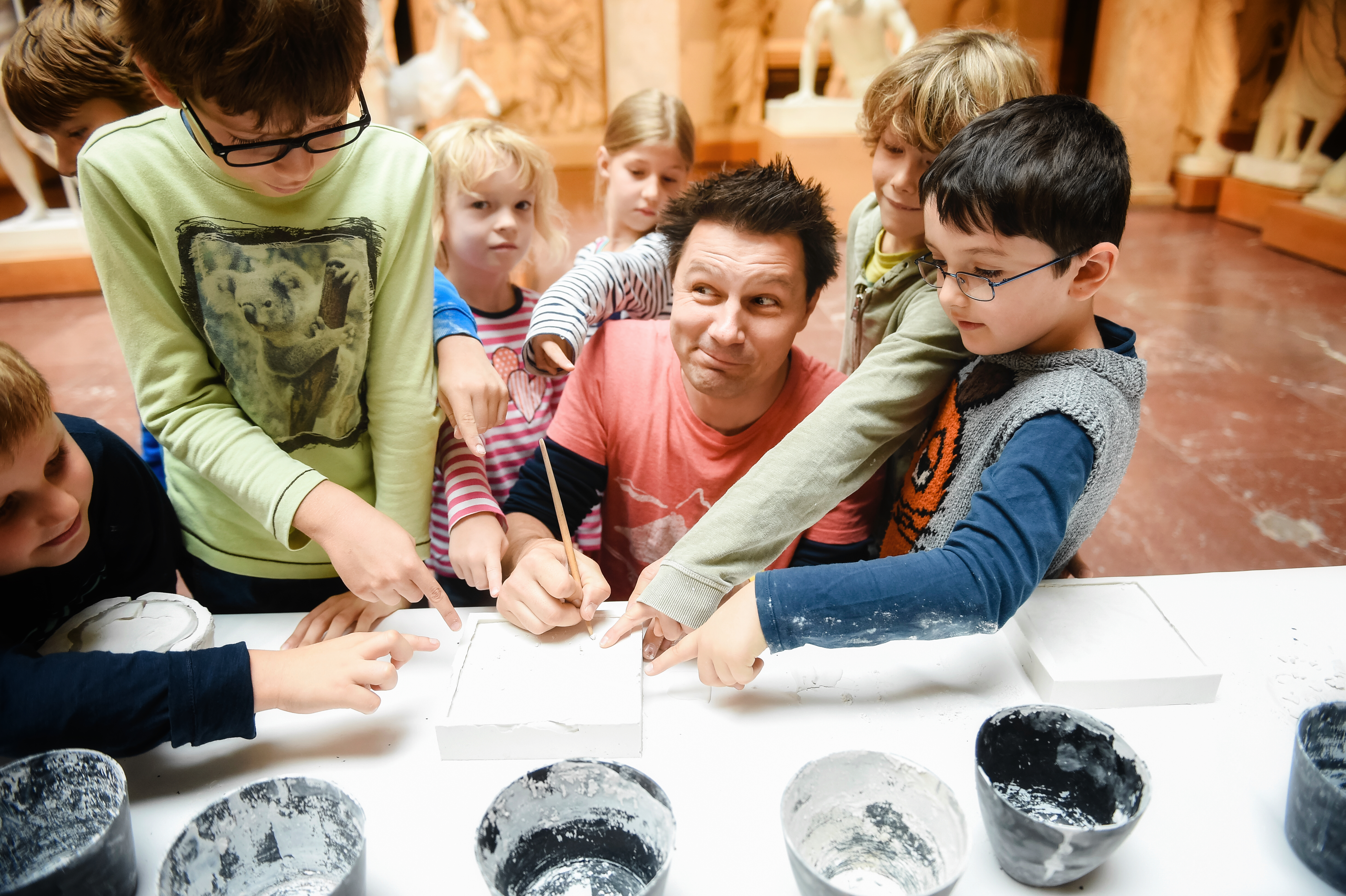 Ein Mann mittleren Alters zusammen mit Kindern vor Gipsutensilien