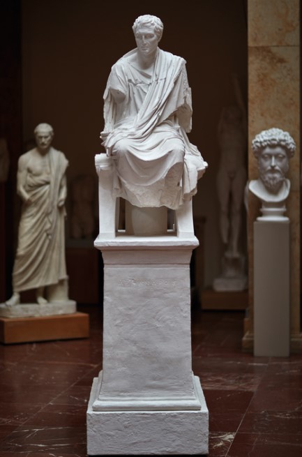 Oben auf einer Säule sitzt ein Mann auf einem Stuhl