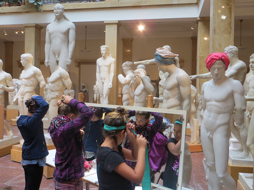 Kinder verkleiden sich vor einem Spiegel, im Hintergrund Statuen